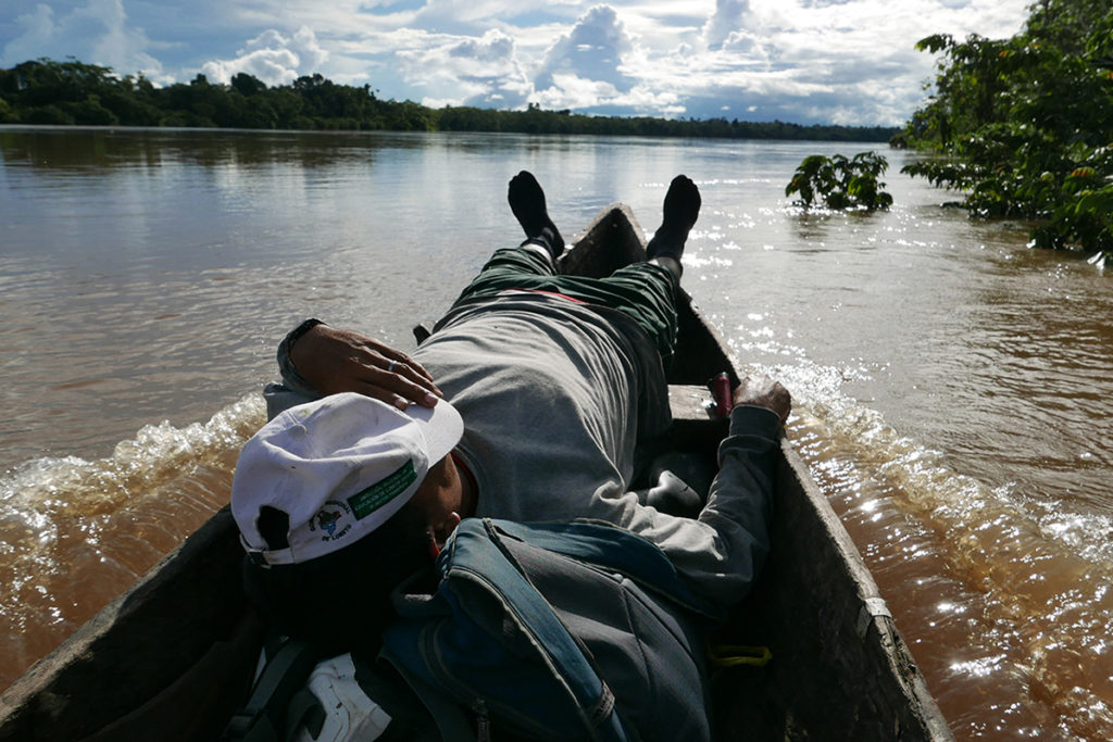 Person lying in boat on a river, with a cap covering their face